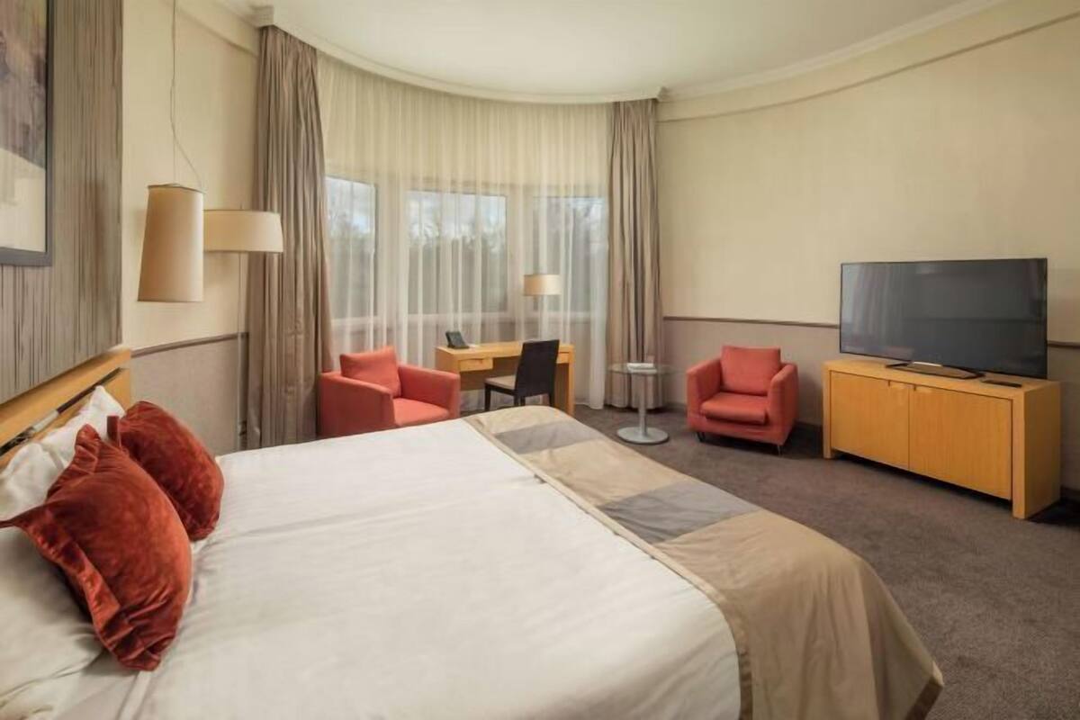 Une chambre d’hôtel avec un grand lit, deux fauteuils, un bureau, une télévision et une petite table.