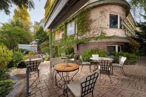 An outdoor patio with tables and chairs, surrounded by greenery and a building with ivy. - Mamaison Hotel Andrassy Budapest (Budapest)