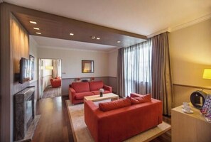Ein Hotelzimmer mit einem roten Sofa, einem Holztisch, einem Fernseher und einem Schreibtisch mit einer Lampe.