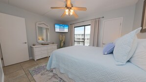 A bedroom with a bed, a ceiling fan, a TV, a dresser, and a window with curtains. - Sugar Beach 2 Bedroom, 2 Bathroom Condo.  4 Pools!  Free Daily Activities! (Orange Beach)
