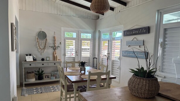 A dining area with a wooden table, white chairs, a hanging light fixture, and a wall with motivational signs. - The Blue Coconut • Pool • Pergola • Steps from Boqueron Beach (Boquerón)