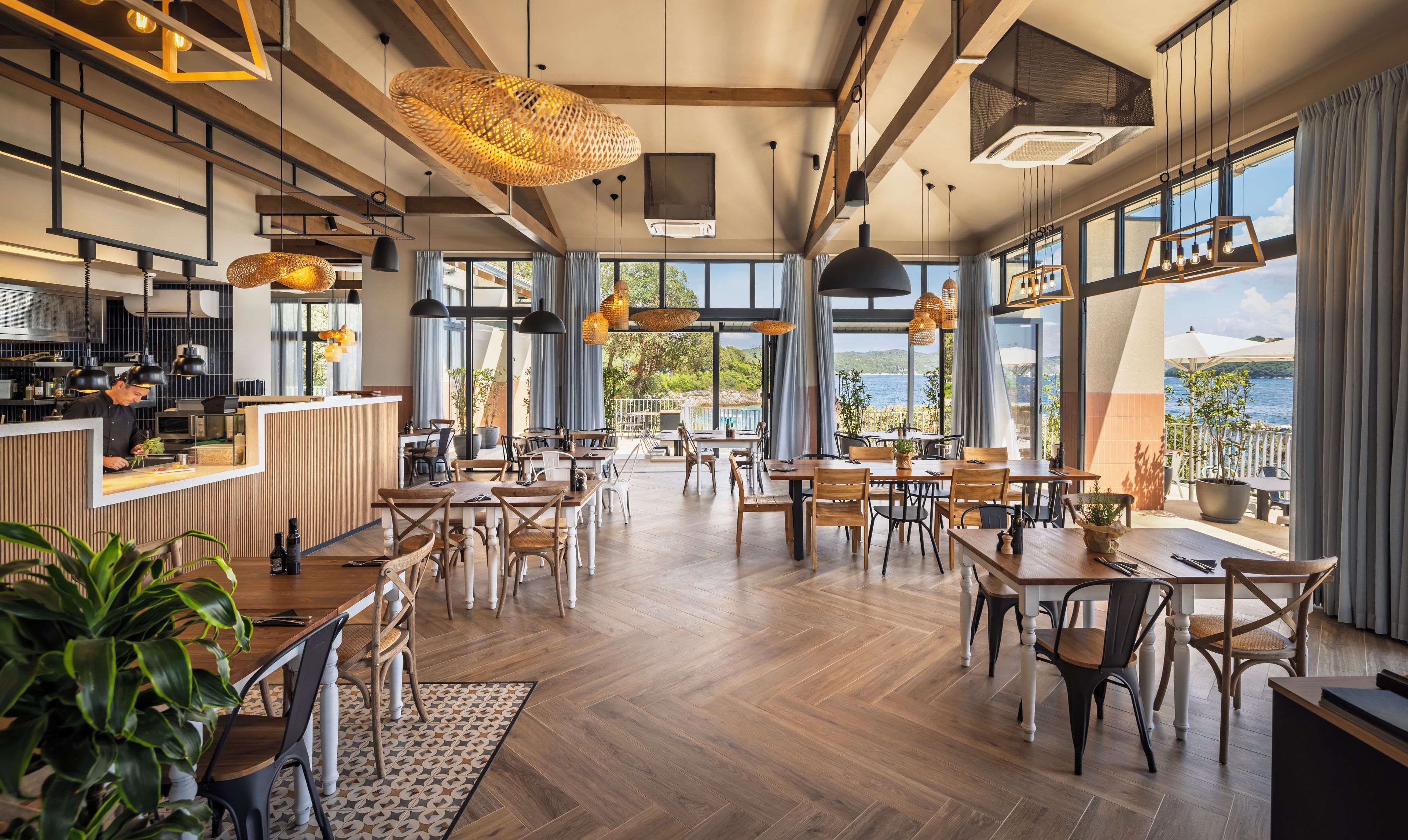 Un restaurante espacioso con suelos de madera, ventanas amplias y lámparas colgantes.