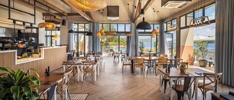 Un restaurante espacioso con suelos de madera, ventanas amplias y lámparas colgantes.