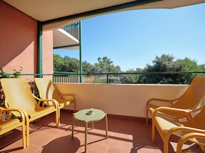 Un balcon avec des fauteuils en osier jaune, une petite table et une vue sur la verdure.