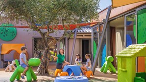 Un'area giochi per bambini con strutture colorate, un albero e un edificio con ampie finestre.