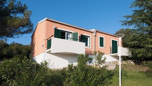 Een huis met twee verdiepingen, een plat dak, groene luiken en een wit balkon.