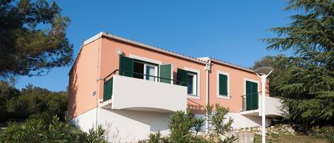 A two-story house with a flat roof, green shutters, and a white balcony.