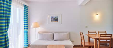 A bedroom with a bed, bedside table, lamp, and a dining area with chairs and a table.