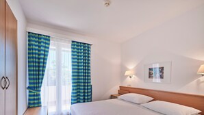 Ein Hotelzimmer mit Bett, Nachttisch, Lampe, einem Bild an der Wand und Vorhängen.