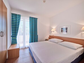 Une chambre d’hôtel avec un lit, une table de chevet, une lampe, un tableau au mur et des rideaux.