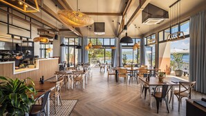 Un'ampia sala ristorante con pavimenti in legno, ampie finestre e lampade a sospensione.