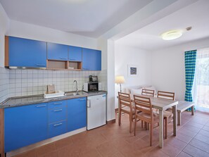 Une cuisine de taille réduite avec des meubles bleus, un réfrigérateur blanc et un coin repas comprenant une table et des chaises.