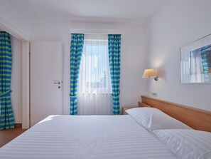 A hotel room with a bed, curtains, a nightstand, a lamp, and a painting on the wall. - Maistra Select Naturist Park Koversada Apartments (Vrsar)