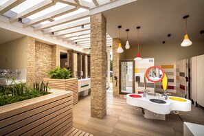 Ein modernes Badezimmer mit einer Holzbank, Steinsäulen und einem farbenfrohen Waschbereich.
