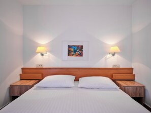 Een hotelkamer met een bed, twee nachtkastjes, twee wandlampen en een lijst met een kunstwerk aan de muur.