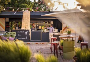 Een terras met zitplaatsen, een krijtbordmenu en diverse flessen op planken.