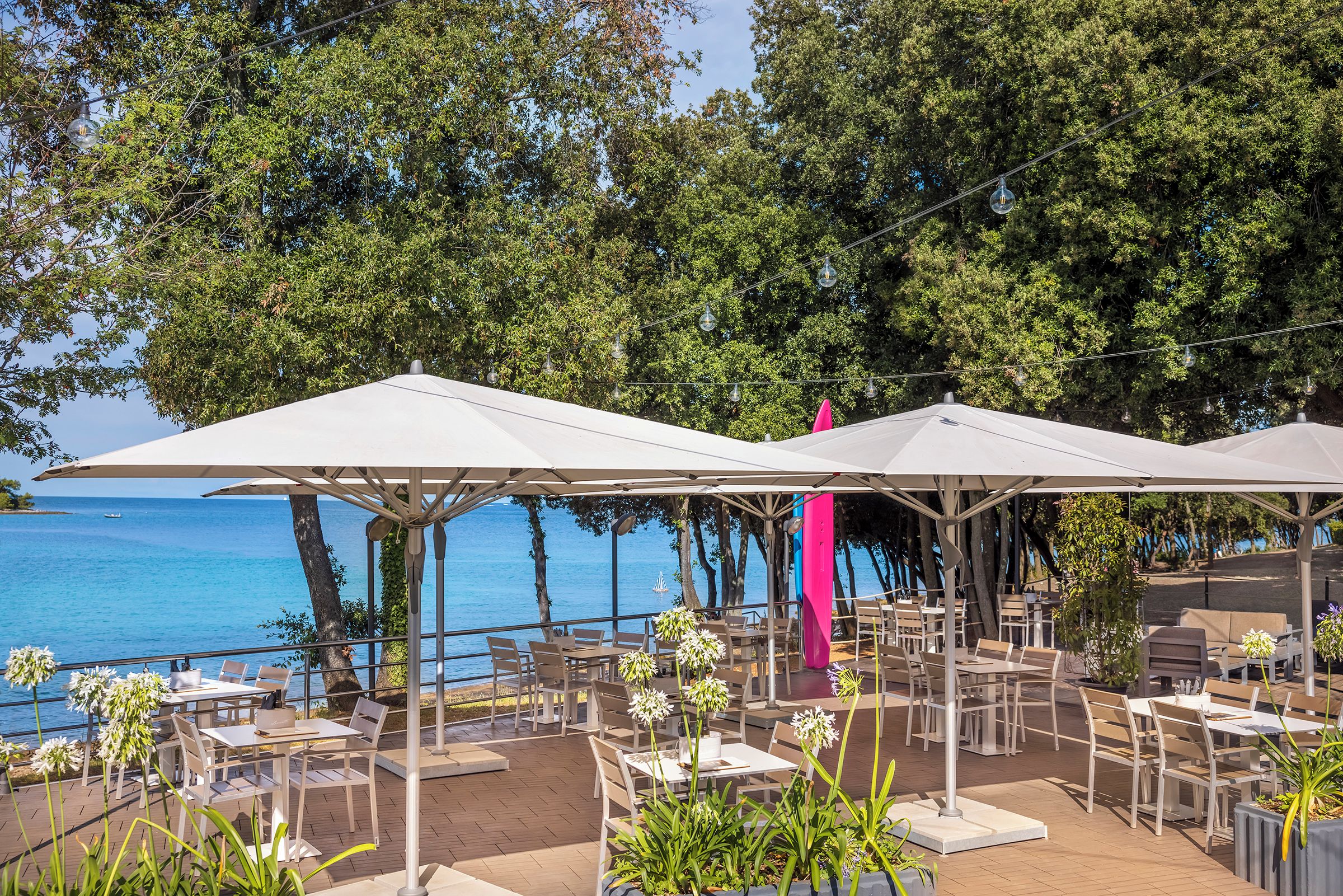 An outdoor dining area with tables and chairs, umbrellas, and a view of the sea.