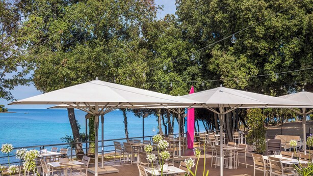 Een terras met tafels en stoelen, parasols en uitzicht op zee.
