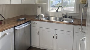 A modern kitchen with white cabinets, a stainless steel sink, and a wooden countertop. - Base Camp Retreat (Glendo)
