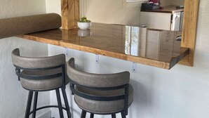 A kitchen with a wooden countertop, two bar stools, a hanging painting, and white cabinets. - Base Camp Retreat (Glendo)