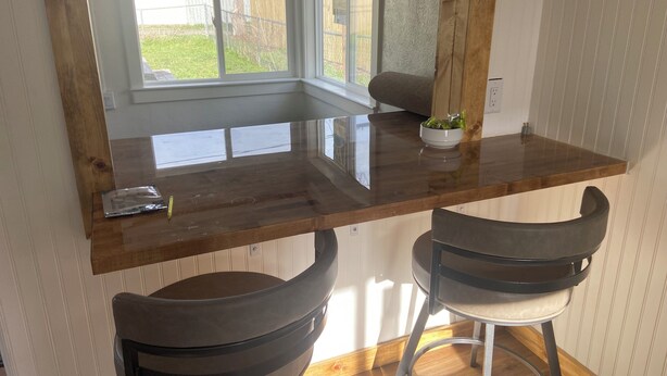 A kitchen with a wooden countertop, two bar stools, and a window with a view of a backyard. - Base Camp Retreat (Glendo)