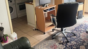 A room with a desk, office chair, and a sofa. There is a washing machine and a radiator in the background. - Comfortable apartment (Montpellier)
