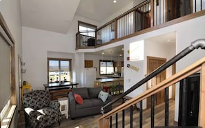 A spacious living area with a staircase, a balcony, and a kitchen in the background.