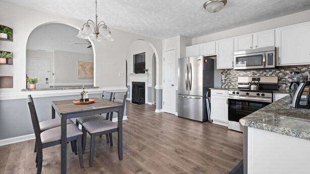 A modern kitchen with white cabinetry, stainless steel appliances, and a wooden dining table. - Quaint Cottage-3BR/2B House with Arcade and Fire Pit in Quiet Part of Hope Mills (Hope Mills)
