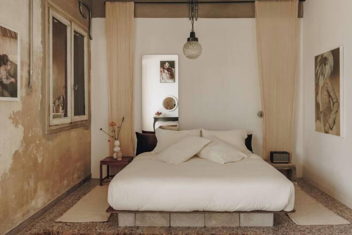 Un dormitorio con cama, mesita de noche, lámpara colgante y ventana.