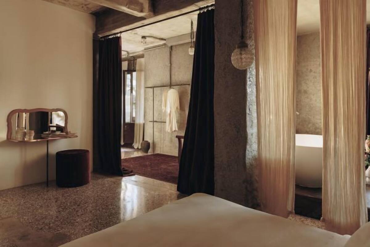 Habitación de hotel con cama, una mesita, espejo y vistas al baño.