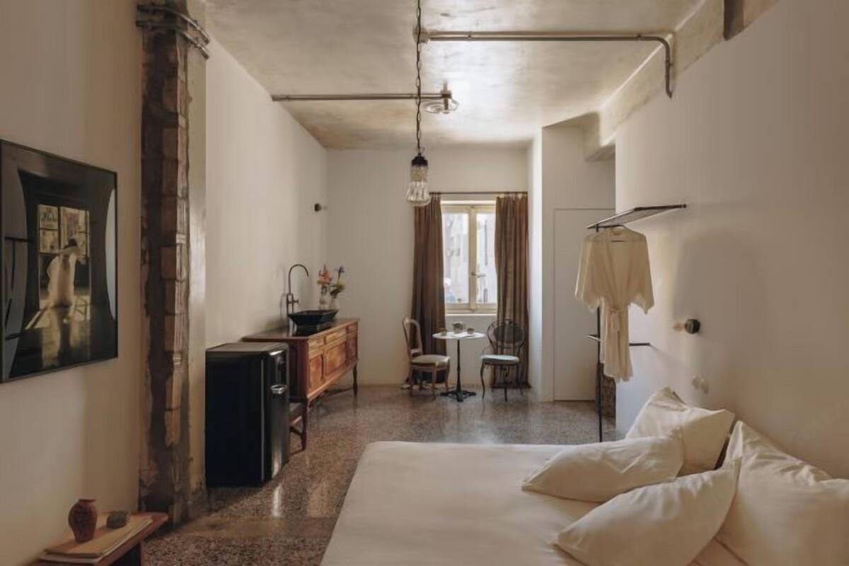 Una habitación con cama, escritorio, silla, lámpara colgante y ventana con cortinas.
