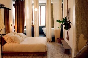 A bedroom with a bed, curtains, a bench, and a potted plant. - Mona Athens (Athens)