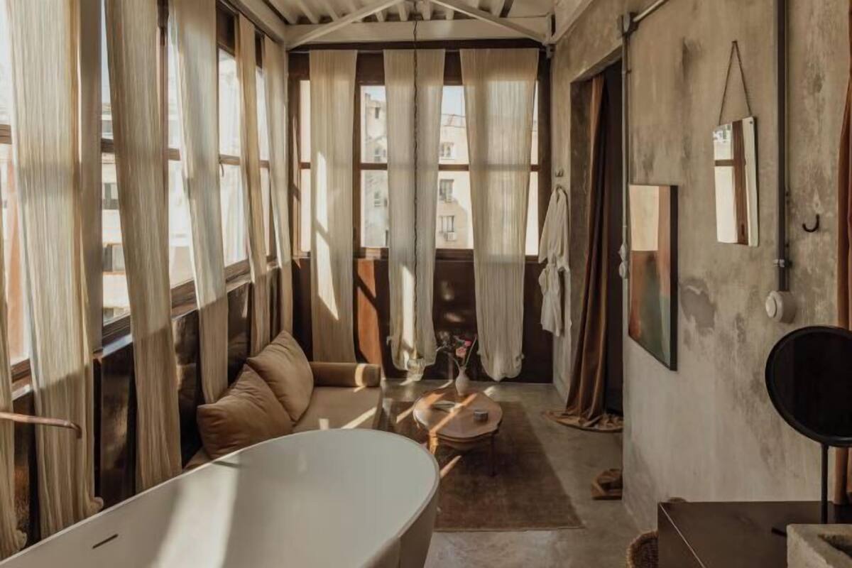 Una habitación con una bañera grande, un sofá, una mesita y cortinas en las ventanas.