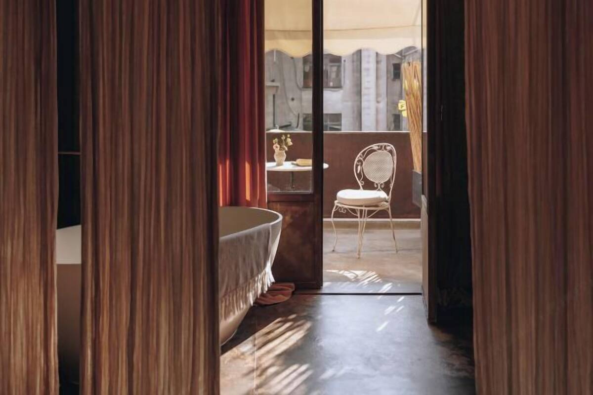 Un baño con una bañera, una silla y una mesita con un florero.