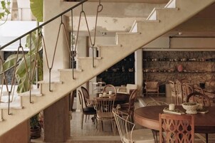 A staircase leading to a dining area with chairs and tables, a stone wall, and hanging plants.