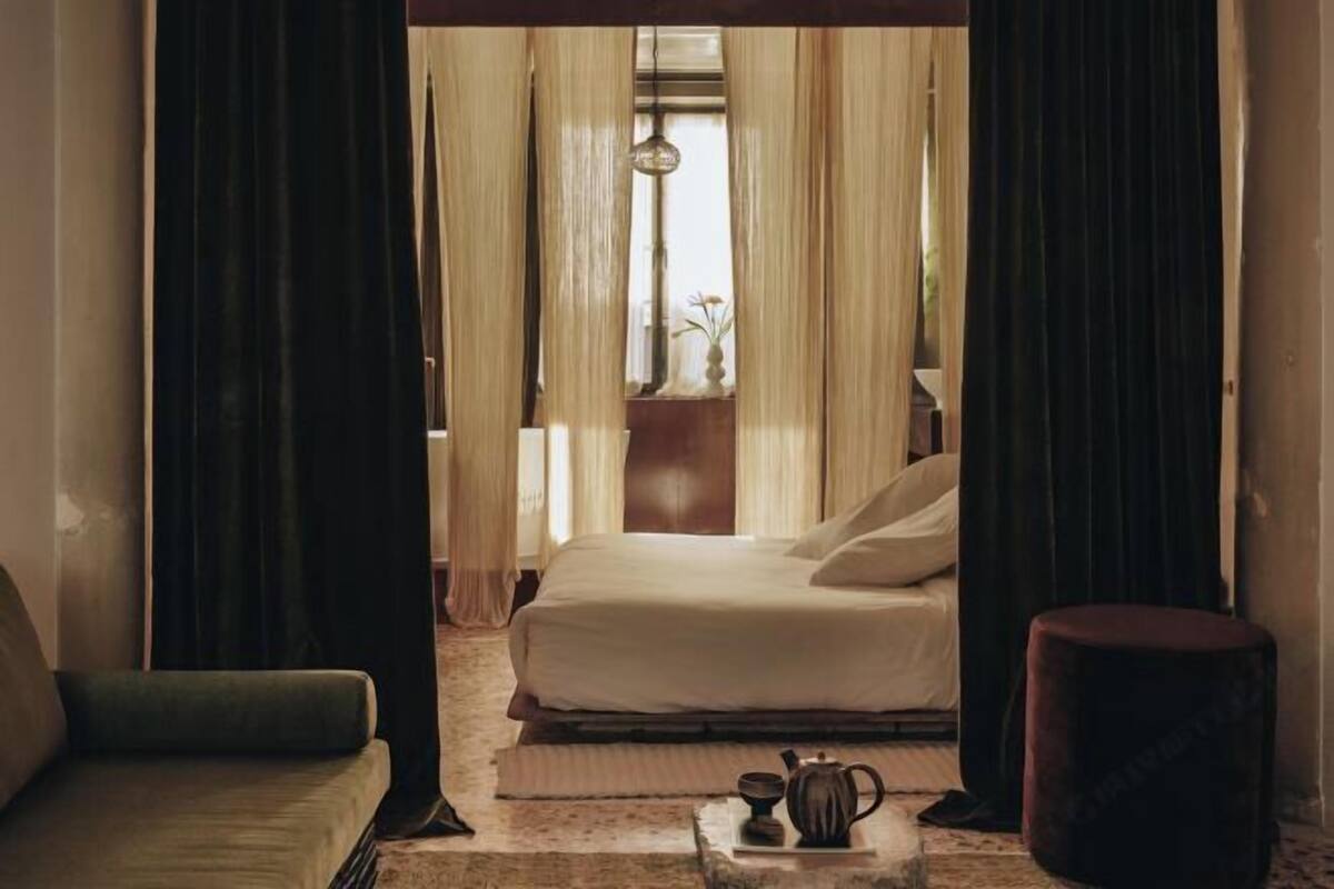 Un dormitorio con cama, una mesita de noche con hervidor y una ventana con cortinas.