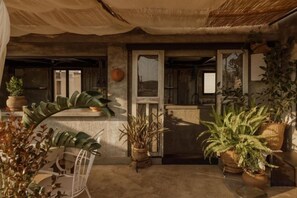 Un'area esterna coperta con piante in vaso, pavimento in cemento e una porta che dà su un ambiente interno.