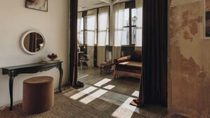A cozy room with a round mirror, a small table, a cushioned bench, and a view through a window with sheer curtains. - Mona Athens (Athens)