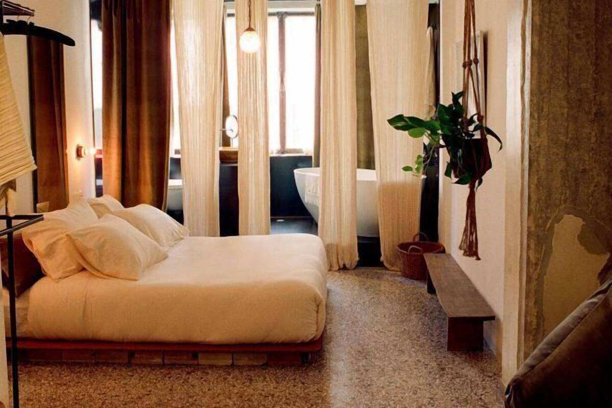 Un dormitorio con cama, un banco, una planta colgante y vistas al baño.