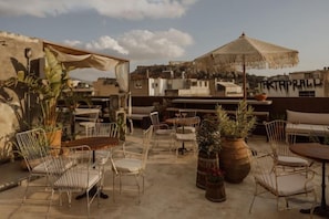 An outdoor patio with metal chairs, a wooden table, and a large umbrella. - Mona Athens (Athens)
