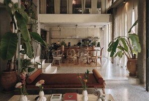 A spacious living area with a sofa, coffee table, and potted plants. A dining area with chairs and a table is visible in the background.