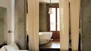 A bedroom with a large bed, a bathroom with a bathtub, and a view of the outside through sheer curtains. - Mona Athens (Athens)