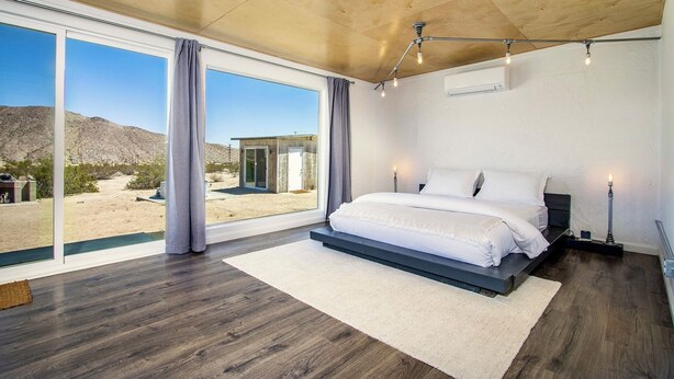 Un dormitorio con un ventanal grande, una cama y vistas a un paisaje desértico.