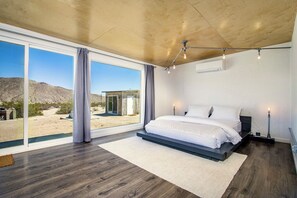 Ein Schlafzimmer mit großem Fenster, einem Bett und Blick auf eine Wüstenlandschaft.
