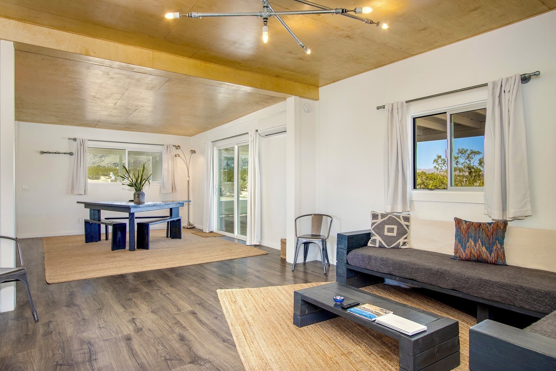 A modern living room with a dark wood floor, a sofa, a coffee table, and a dining area with a table and chairs.