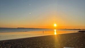 A beach with a sunset, calm sea, and a distant city skyline.