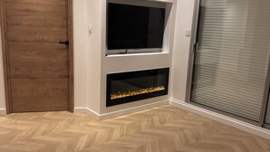 A modern living room with a wooden door, a flat-screen TV mounted above a fireplace, and a sliding glass door.