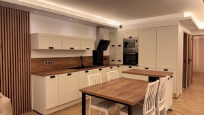 A modern kitchen with white cabinetry, a wooden countertop, and a dining area with white chairs.