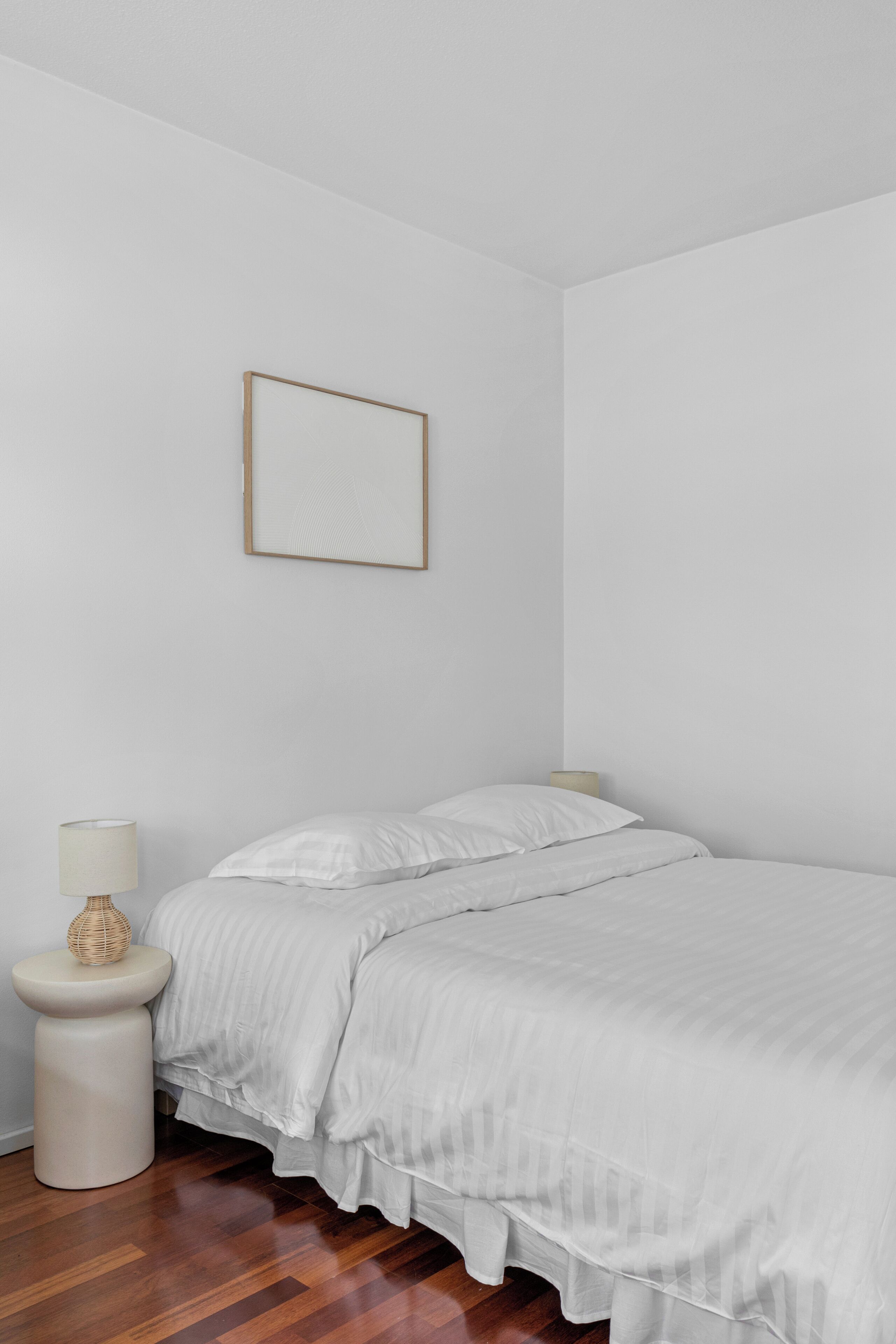 Ein Schlafzimmer mit einem Bett, einem Nachttisch, einer Lampe und einem gerahmten Bild an der Wand.
