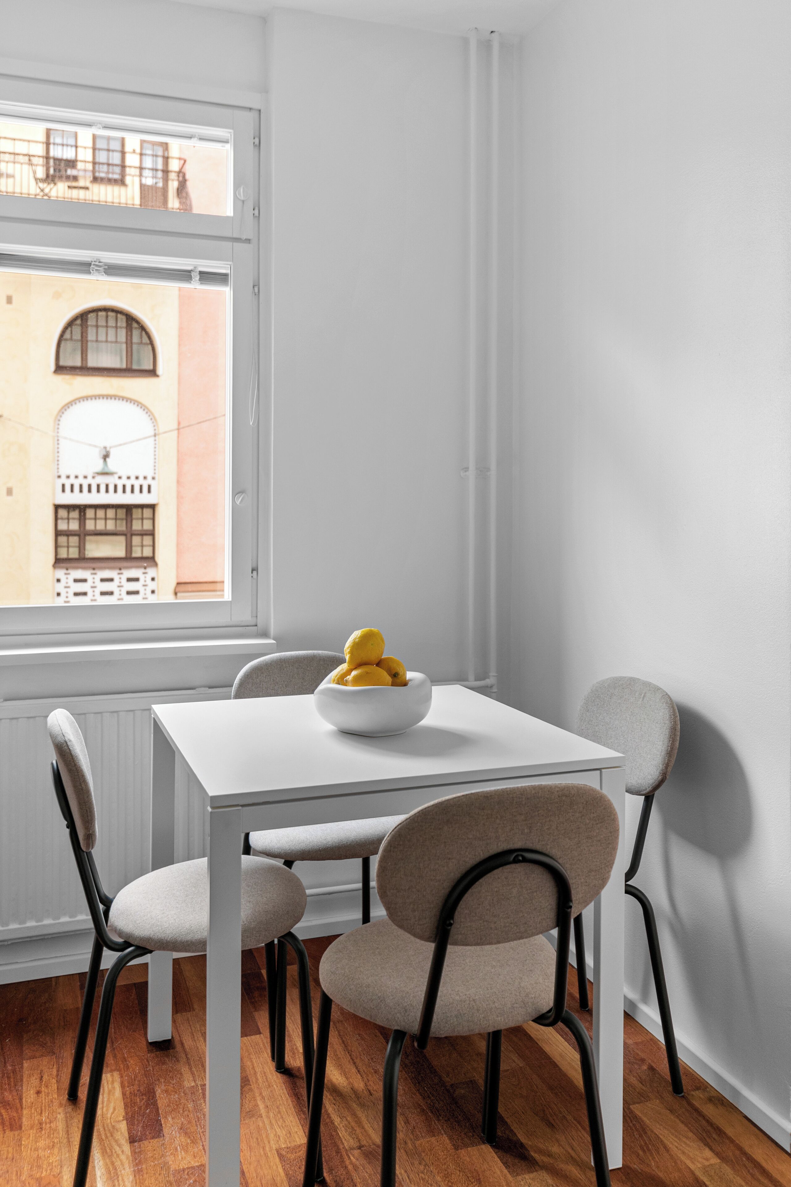 Un comedor con una mesa blanca, cuatro sillas y un cuenco de limones sobre la mesa.